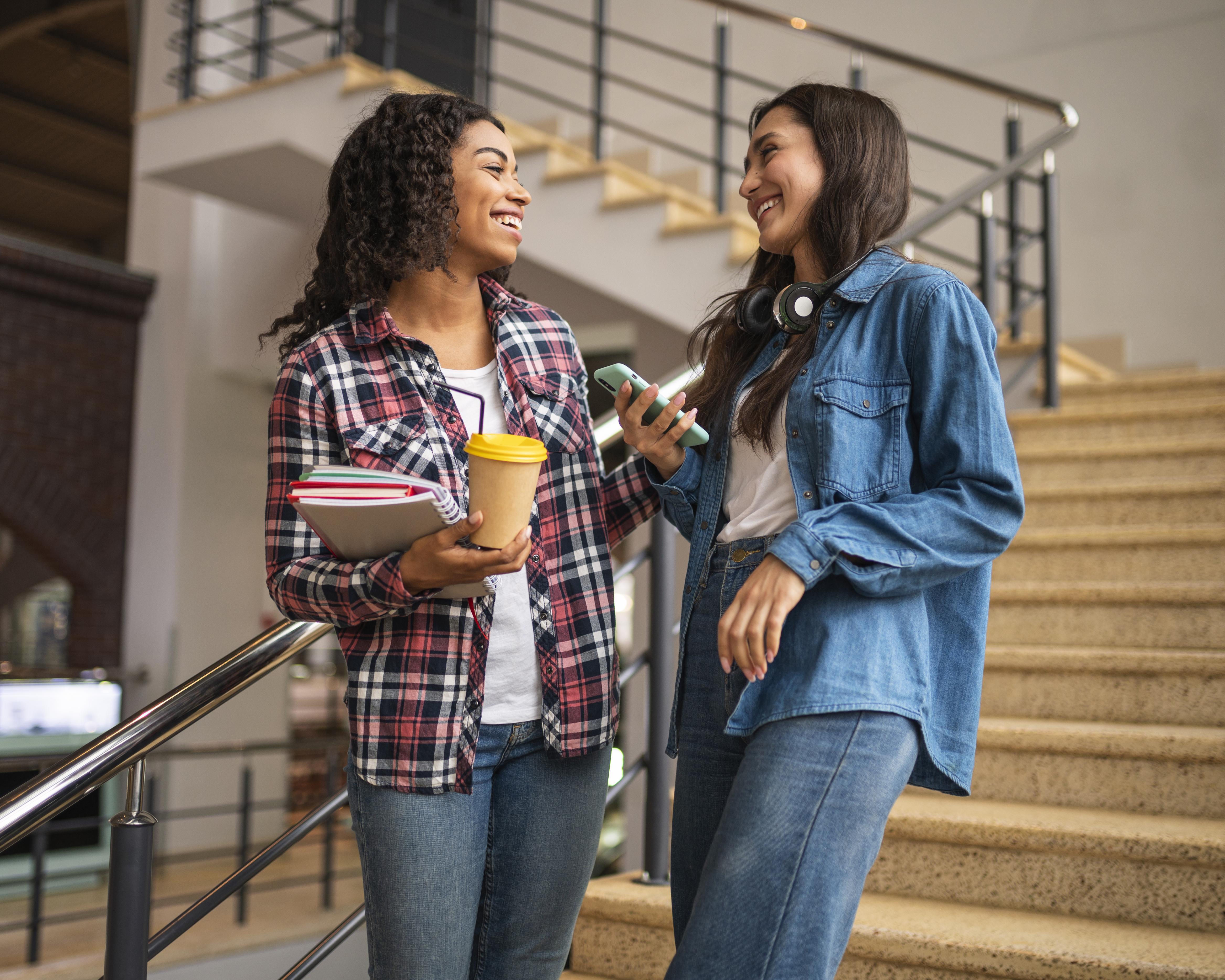 Two female friends talking on the staircase in a university building.