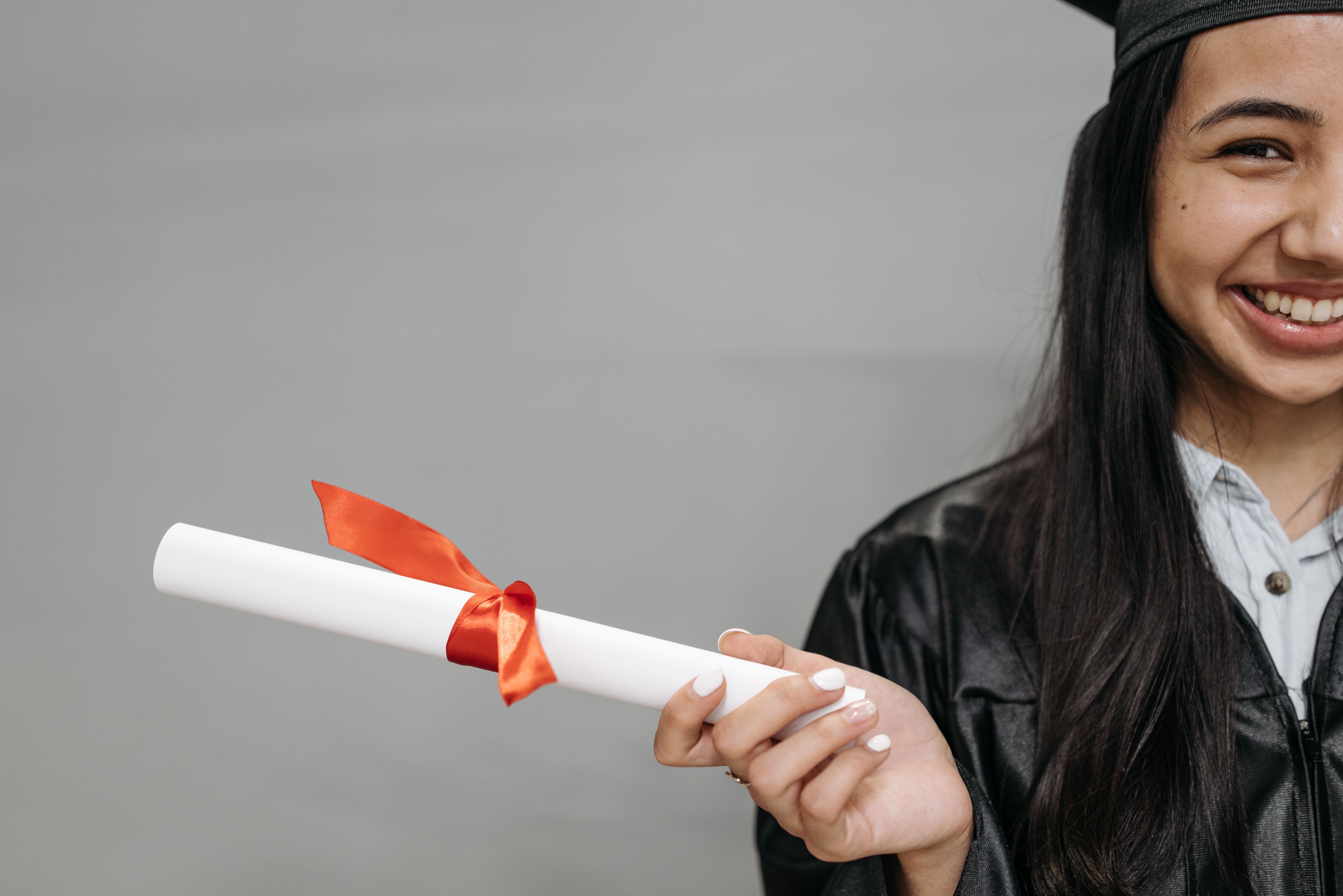 A female high school graduate smiling while holding a white diploma wrapped with an orange bow.